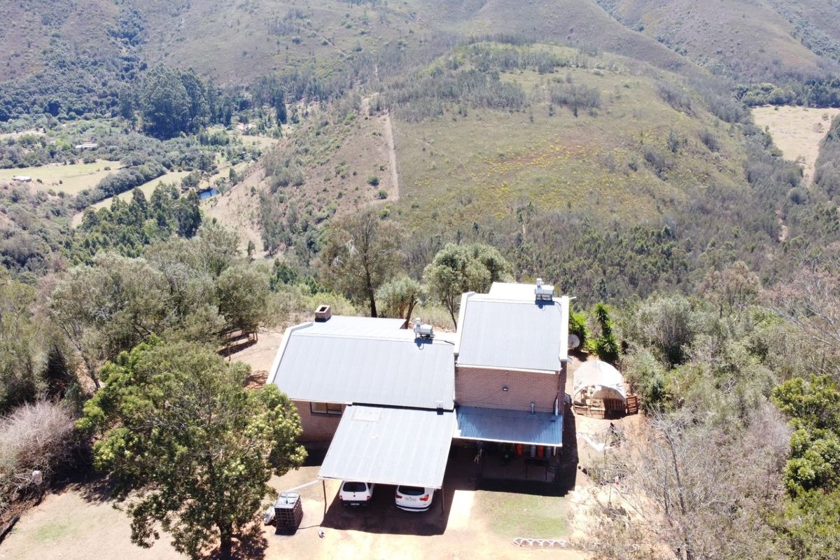 Aerial view of a rural property featuring a main dwelling with a metal roof, attached carport, and expansive surrounding landscape.
