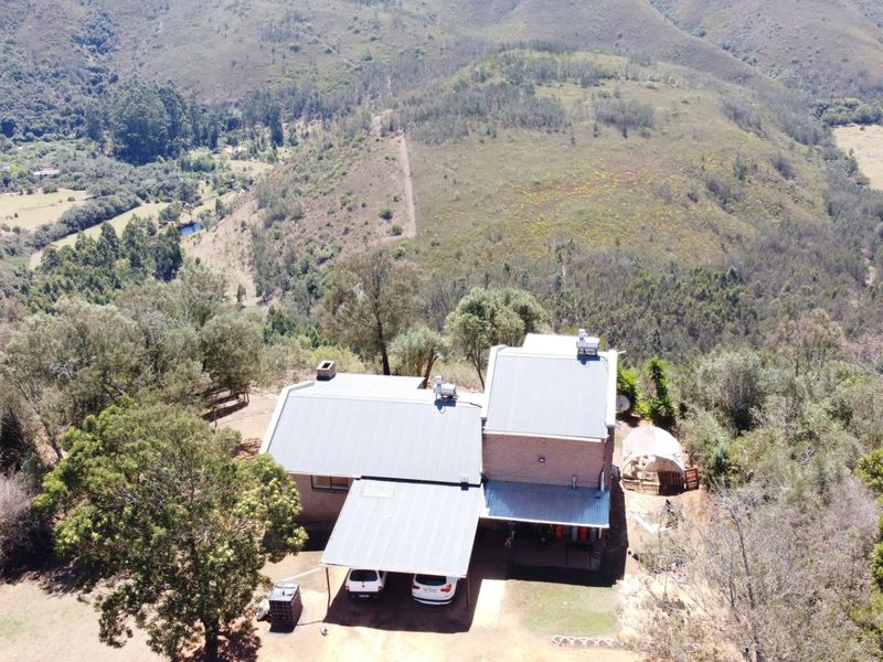 Aerial view of a rural property featuring a main dwelling with a metal roof, attached carport, and expansive surrounding landscape.