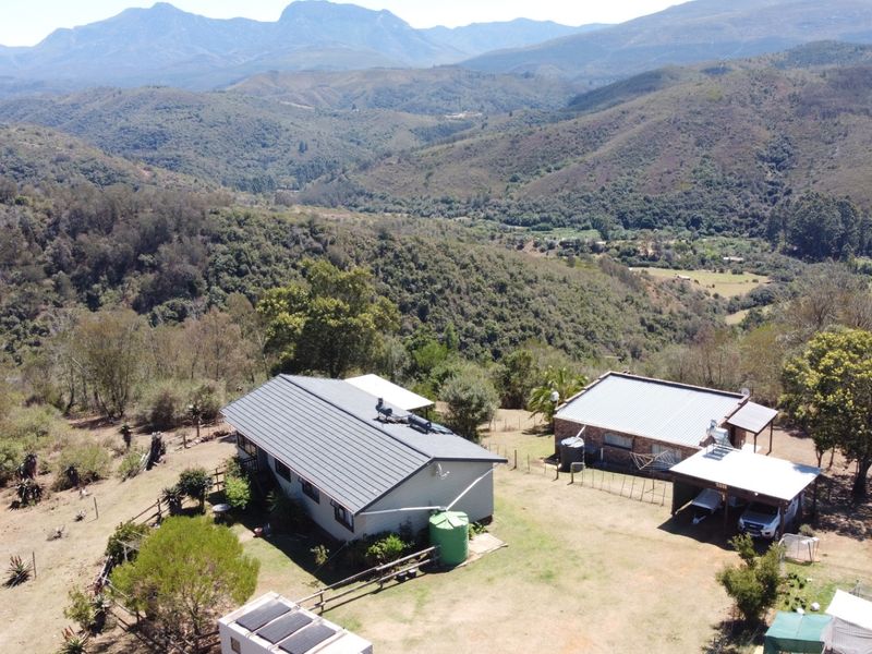 Aerial view of a farm property featuring multiple buildings, metal roofing, solar water heating systems, and expansive mountain landscape views.
