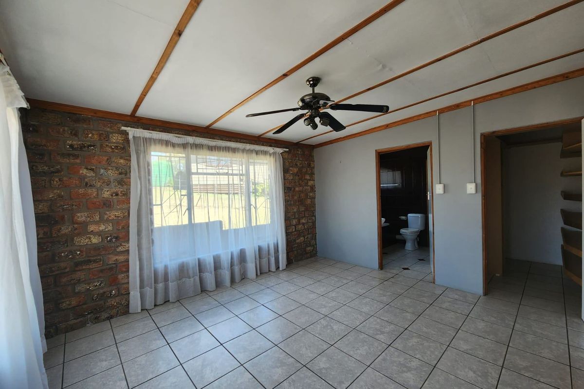 Spacious living area featuring exposed brick walls, tiled flooring, and timber ceiling beams, with direct access to an adjoining bathroom.