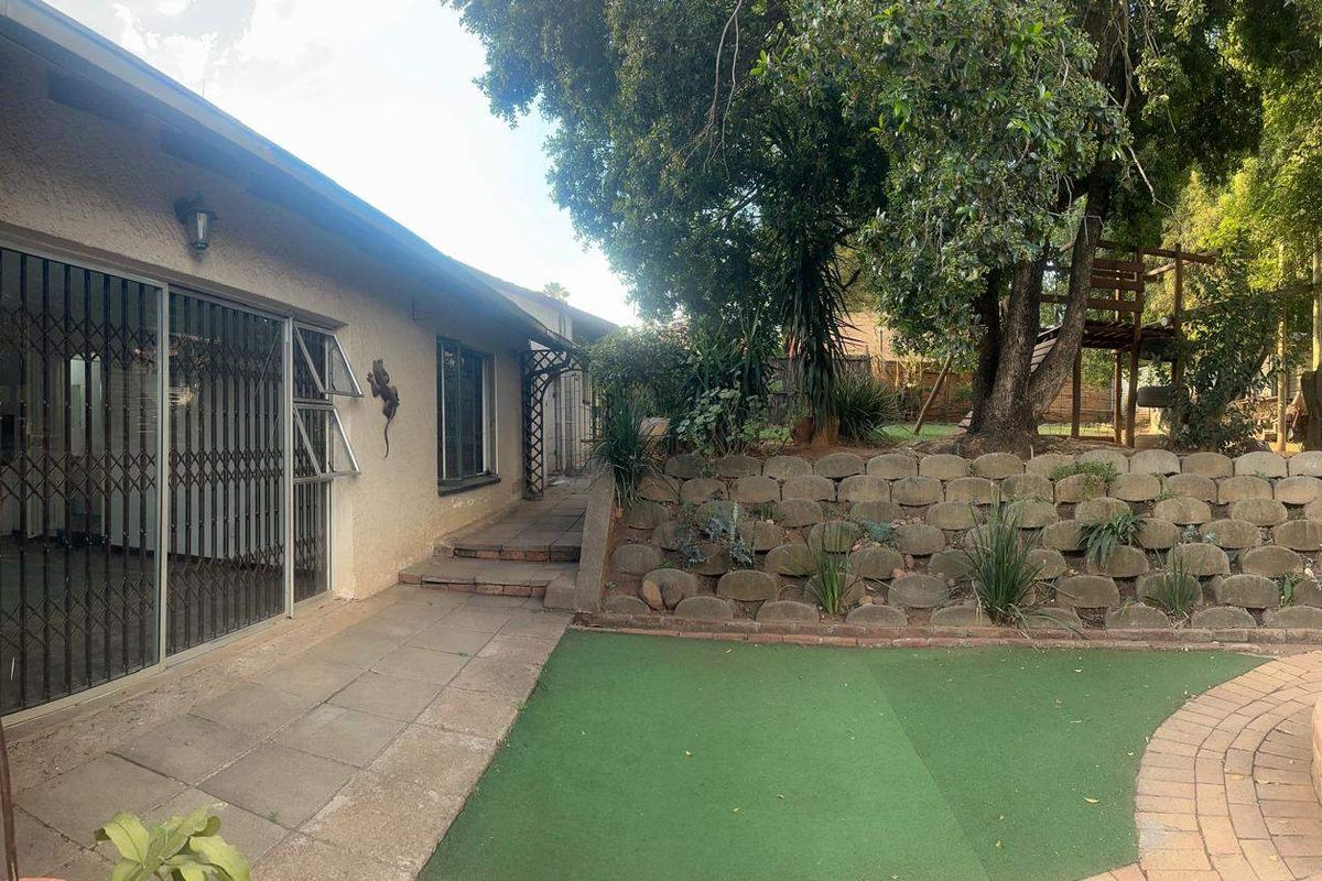 Rear exterior view featuring a paved patio area, artificial lawn, and a tiered retaining wall leading to a garden space.