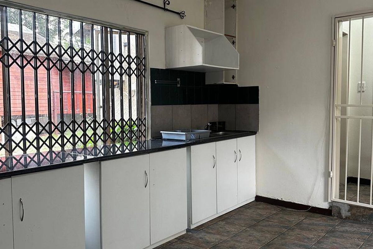 A functional kitchen space featuring built-in white cabinetry, dark granite countertops, tiled flooring, and security features on the window and door.