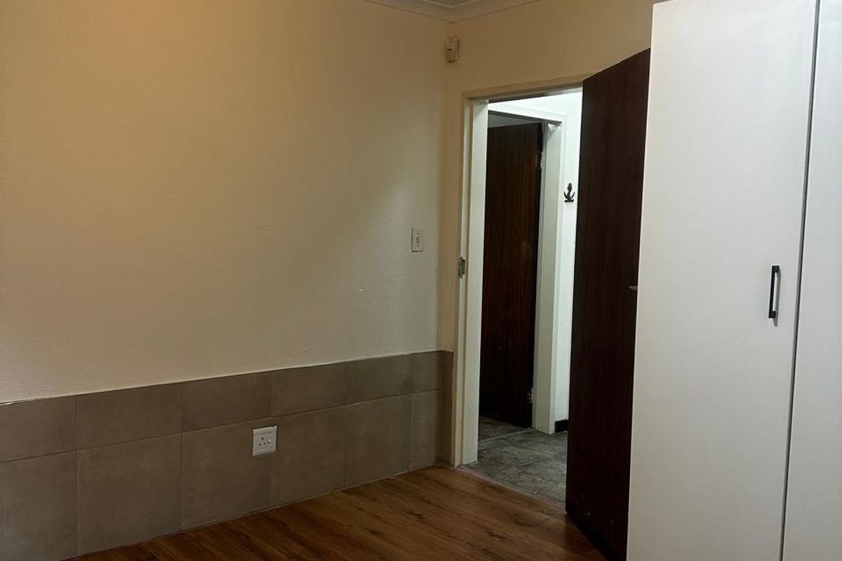 A simple bedroom featuring laminate flooring, a built-in wardrobe, and tiled wall skirting, providing a functional and neutral space.