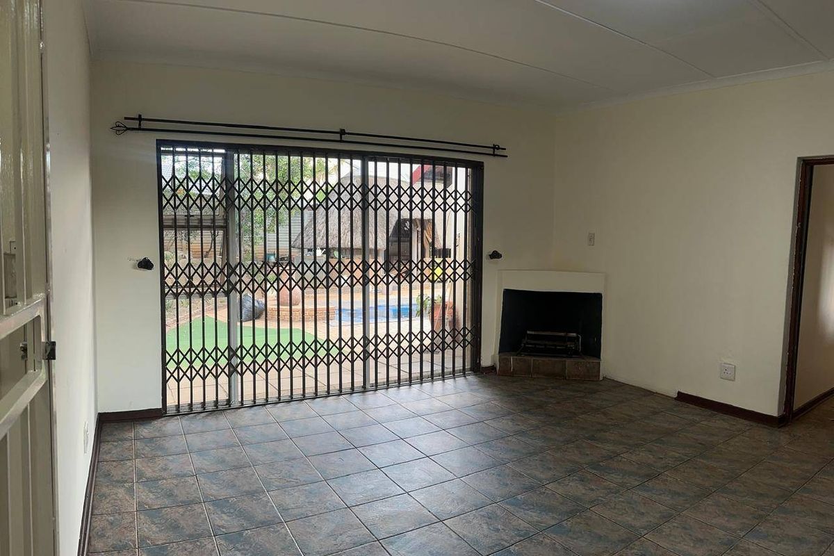 Spacious living room featuring tiled flooring, a built-in fireplace, and a sliding glass door with a security gate leading to the outdoor area.