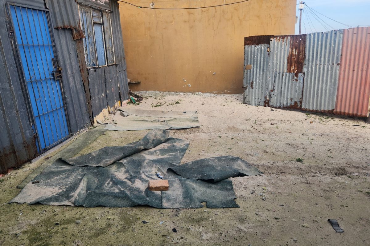 A view of the rear exterior area featuring a corrugated metal structure and basic fencing on a sandy plot.