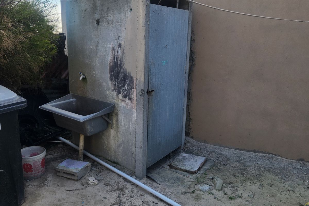 An outdoor utility structure featuring a concrete enclosure and an external sink with exposed plumbing connections.
