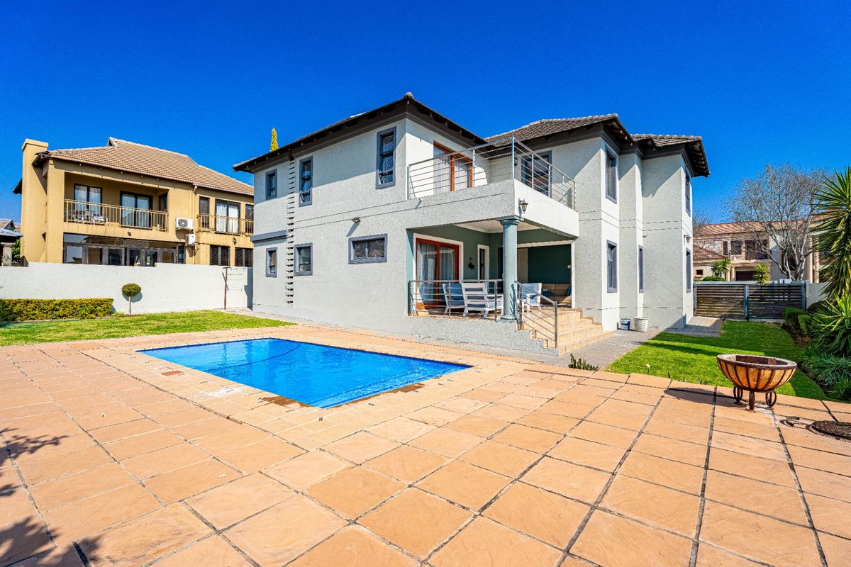 Rear view of the house featuring a swimming pool, paved patio area, elevated balcony, and a well-maintained garden.