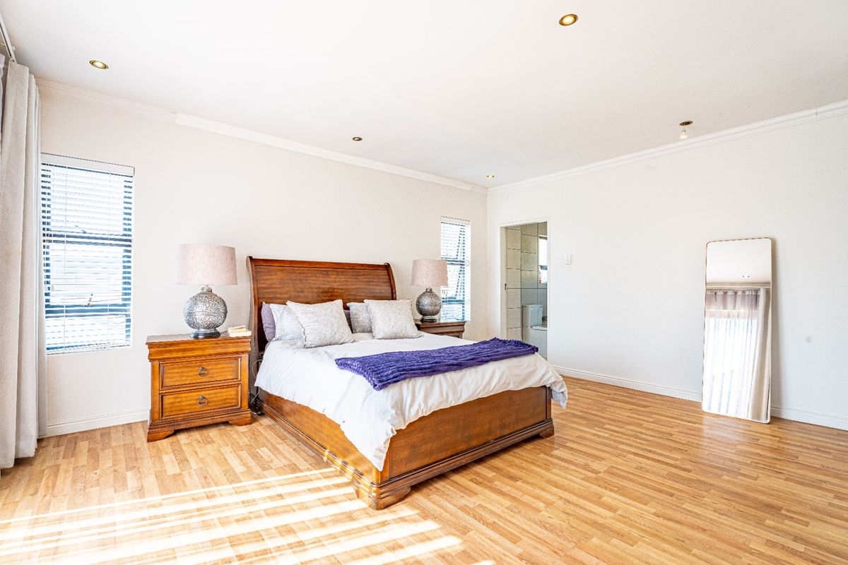 Spacious bedroom featuring warm laminate flooring, recessed downlighting, and direct access to an en-suite bathroom, creating a bright and comfortable living space.