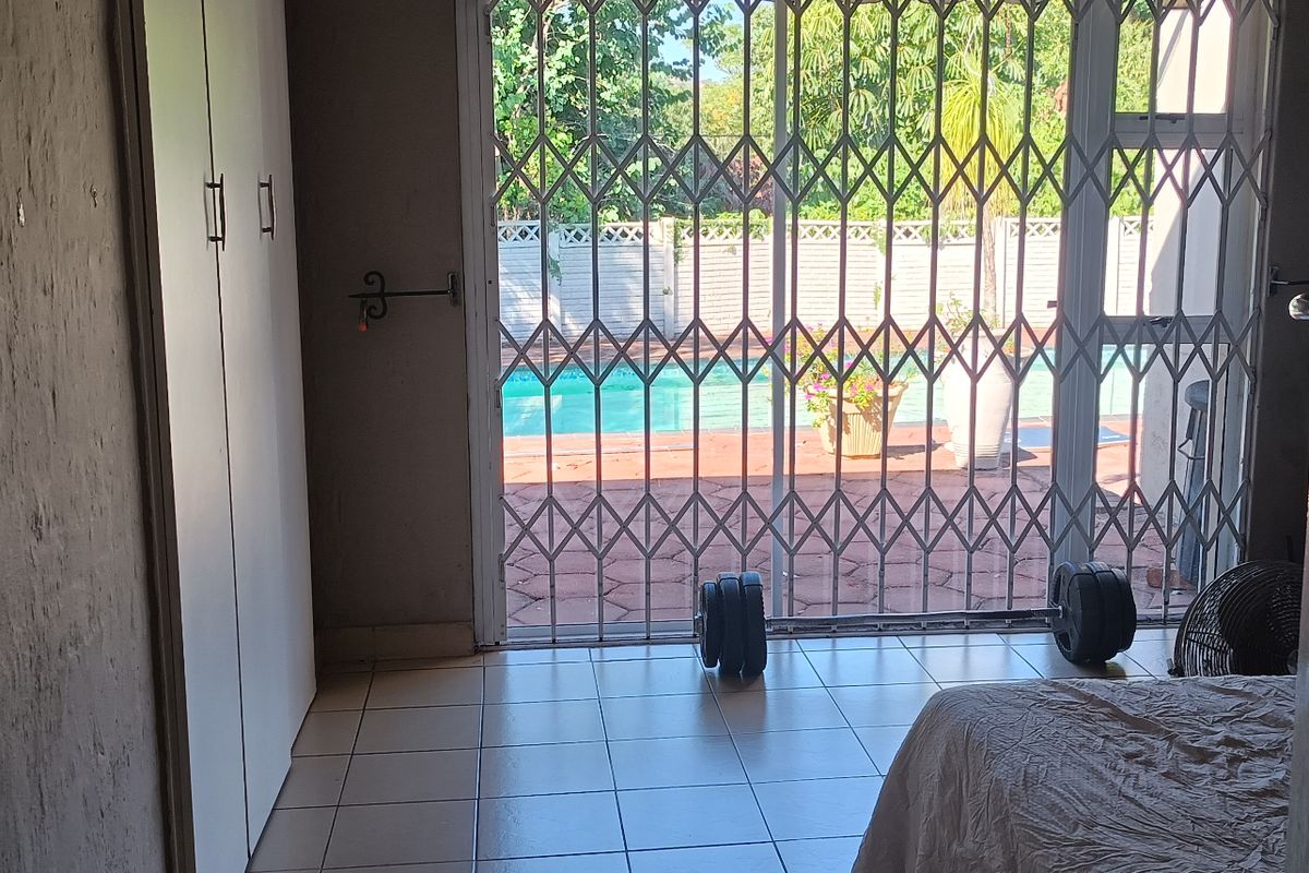 Bedroom featuring built-in cupboards, tiled flooring, and a sliding glass door with a security gate providing direct access to the pool area.