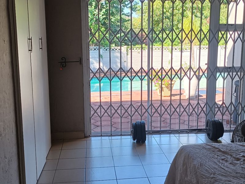 Bedroom featuring built-in cupboards, tiled flooring, and a sliding glass door with a security gate providing direct access to the pool area.