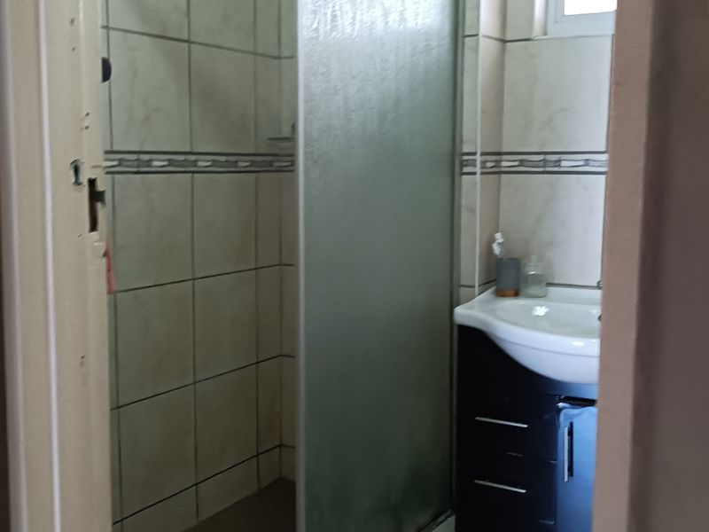 A compact bathroom featuring a shower enclosure, vanity basin, and tiled walls, showing signs of wear on the door frame.
