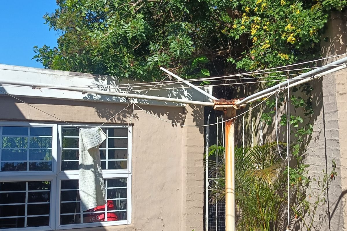 A rear exterior area featuring a weathered rotary clothesline, masonry walls, and windows fitted with security bars.