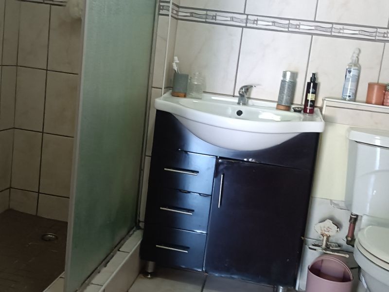 A functional bathroom featuring a vanity cabinet with basin, a shower enclosure, and a standard toilet with tiled walls.