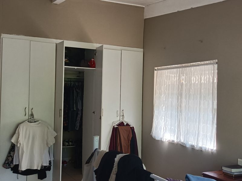 A bedroom featuring built-in cupboards and a window with natural light, requiring cosmetic updates to the wall finishes.