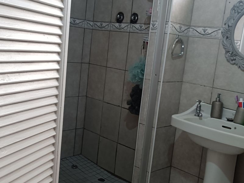 A functional bathroom featuring a pedestal basin, shower enclosure, and tiled walls, requiring some cosmetic updates to improve its overall aesthetic.