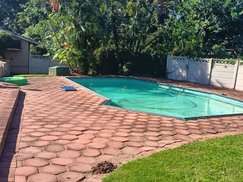 Outdoor pool area featuring a swimming pool, paved patio space, and perimeter boundary wall, set within a garden environment.