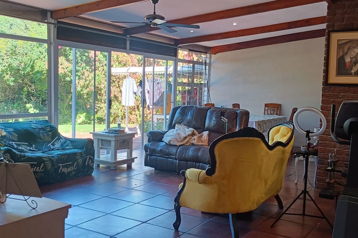 Spacious living area featuring exposed timber ceiling beams, a brick fireplace, and large sliding glass doors providing direct access to the garden.