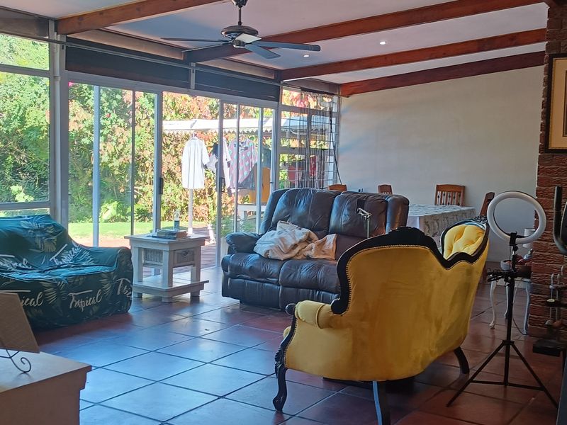 Spacious living area featuring exposed timber ceiling beams, a brick fireplace, and large sliding glass doors providing direct access to the garden.
