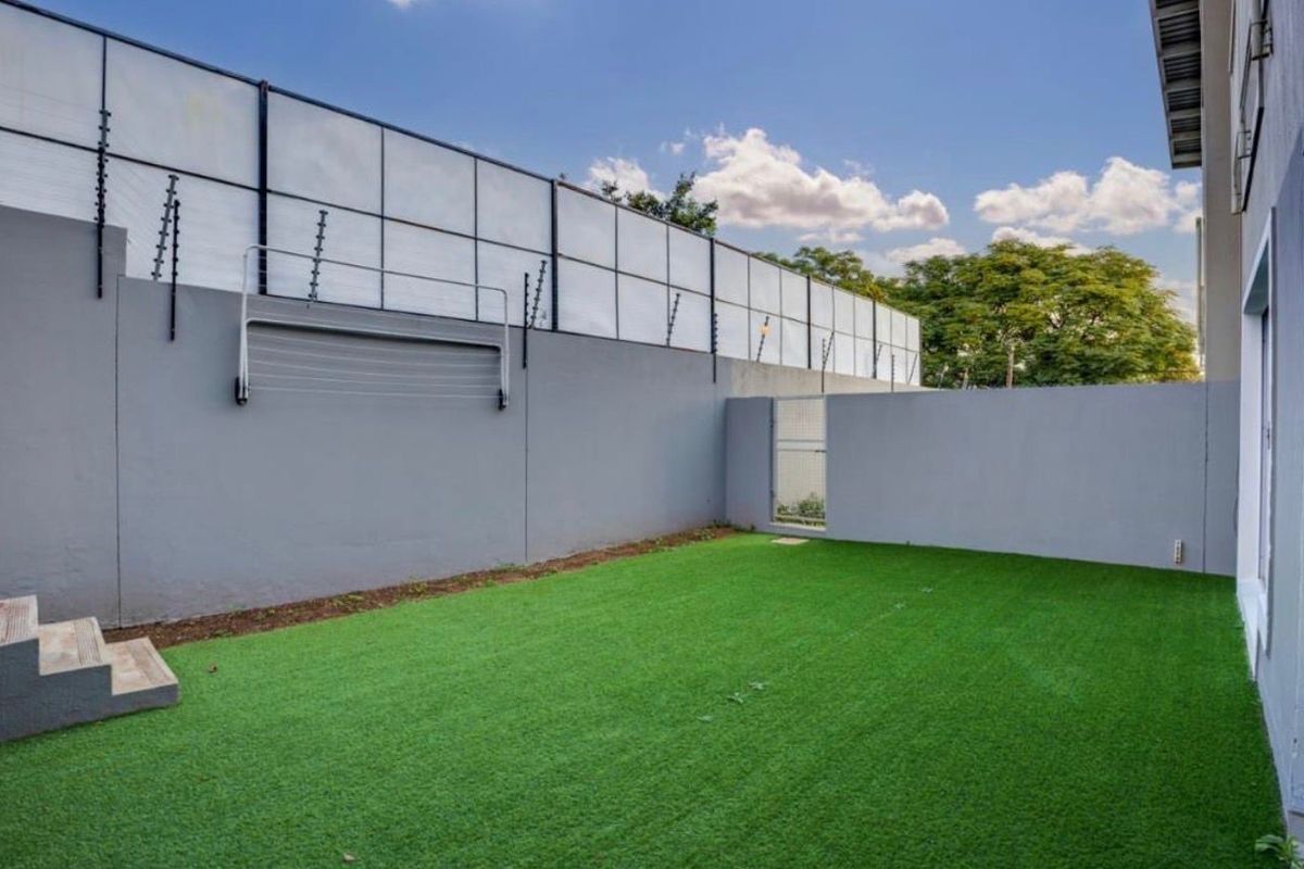 A private rear courtyard featuring artificial turf, a secure perimeter wall with electric fencing, and a wall-mounted clothesline.