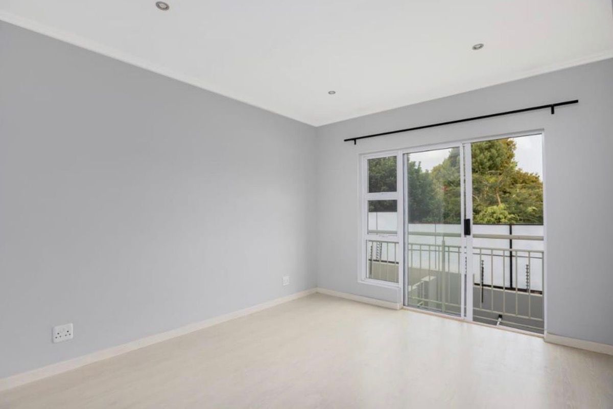 A bright, empty bedroom featuring neutral walls, laminate flooring, recessed lighting, and a sliding glass door providing access to a balcony.