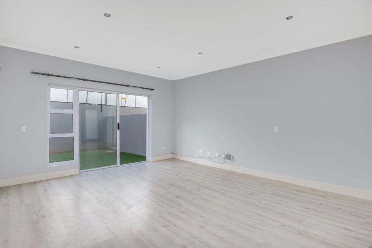 A bright, empty living room featuring light-toned laminate flooring, recessed downlights, and a sliding glass door providing access to the rear outdoor area.
