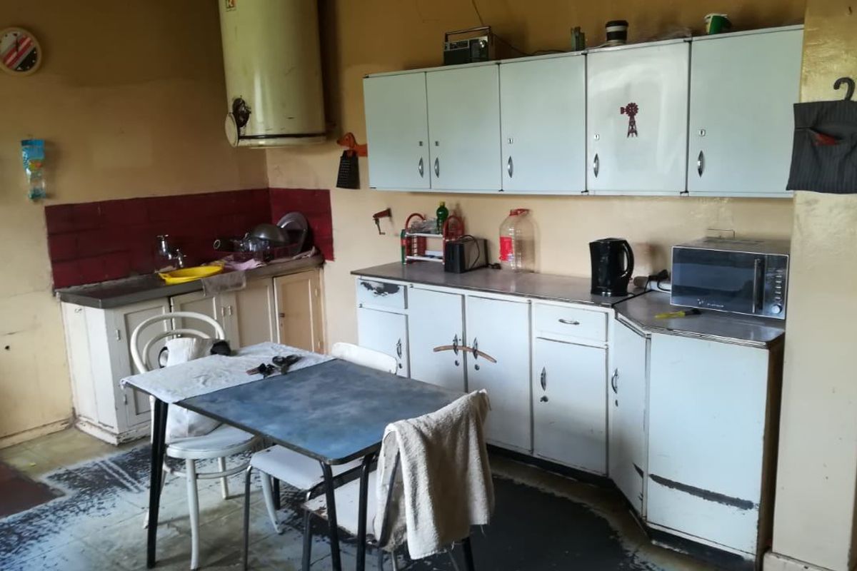 A dated kitchen featuring original built-in cabinetry, a stainless steel sink, and tiled splashback, requiring significant renovation to modernize the space.