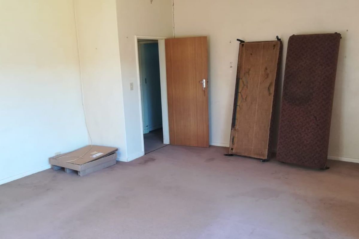 An empty living room space featuring worn carpeting and visible wall imperfections, offering a blank canvas for renovation and interior updates.