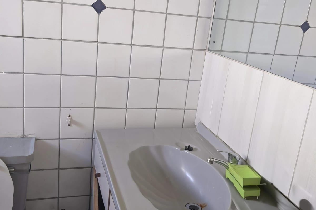 A dated bathroom featuring a vanity unit with an integrated sink, wall-mounted mirror, and white ceramic wall tiling.
