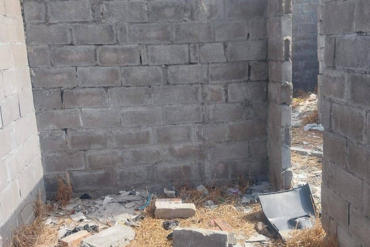 An unfinished room structure featuring exposed concrete block walls and significant construction debris on the ground.