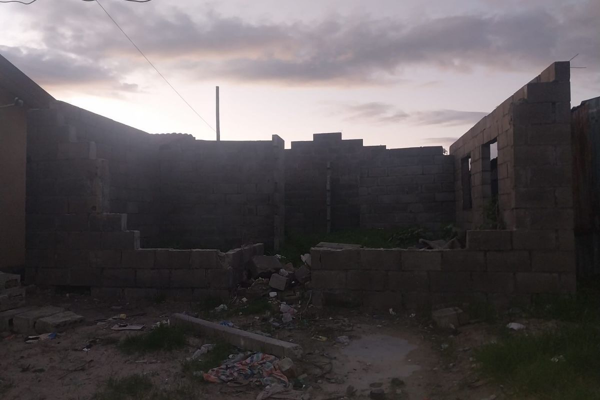 An unfinished residential structure featuring exposed concrete block walls on a vacant plot of land.