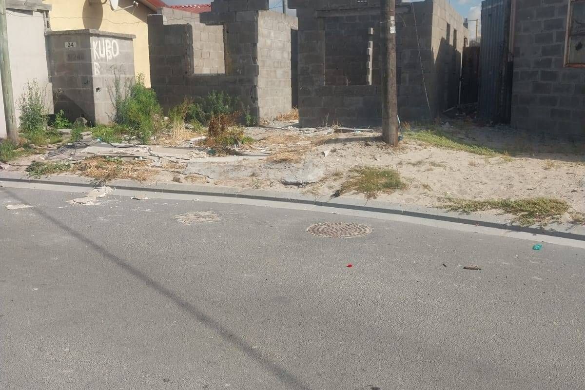 A view of a residential plot featuring an incomplete concrete block structure under construction, situated along a paved street.