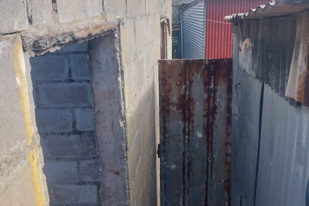 A narrow exterior passage featuring unfinished concrete block walls and corrugated metal structures with a weathered metal door.