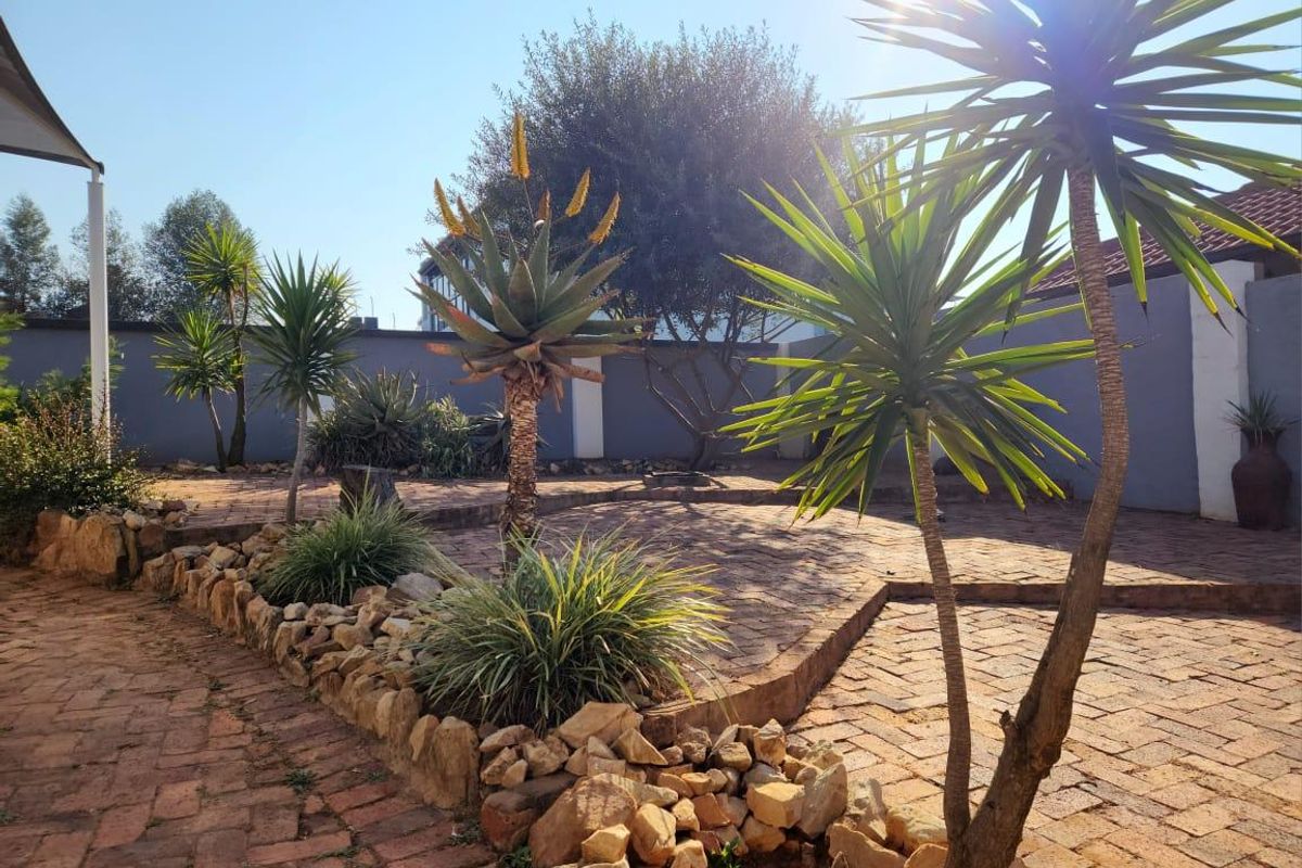 A well-maintained garden area featuring brick paving, a stone retaining wall, and established landscaping against a solid boundary wall.