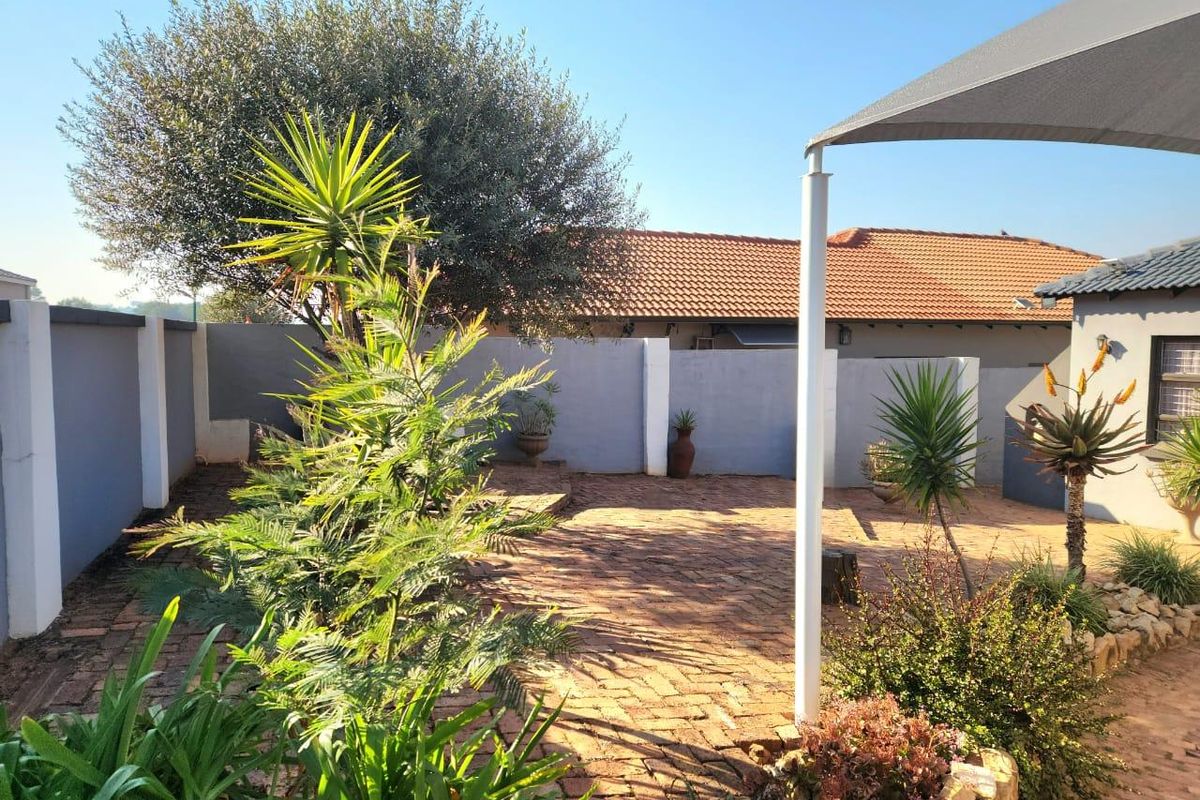 A private rear courtyard featuring brick paving, established garden beds, and a shade sail structure, providing a low-maintenance outdoor living space.