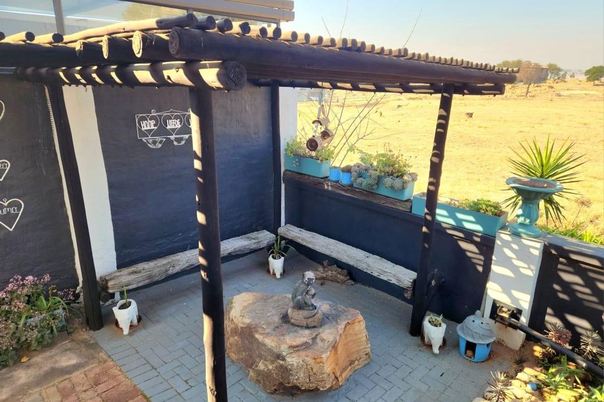 A rustic outdoor patio area featuring a timber pergola, built-in bench seating, and paved flooring, overlooking an open landscape.