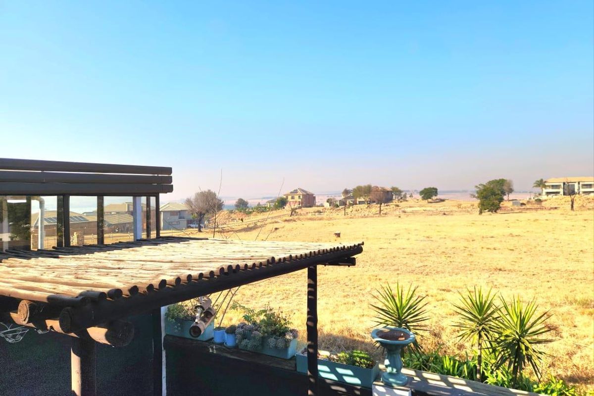 An elevated view overlooking a dry landscape and neighbouring properties, featuring a timber pergola structure in the foreground.