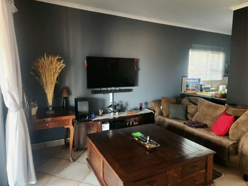 A living room featuring dark grey accent walls, tiled flooring, and a view through to the kitchen area.