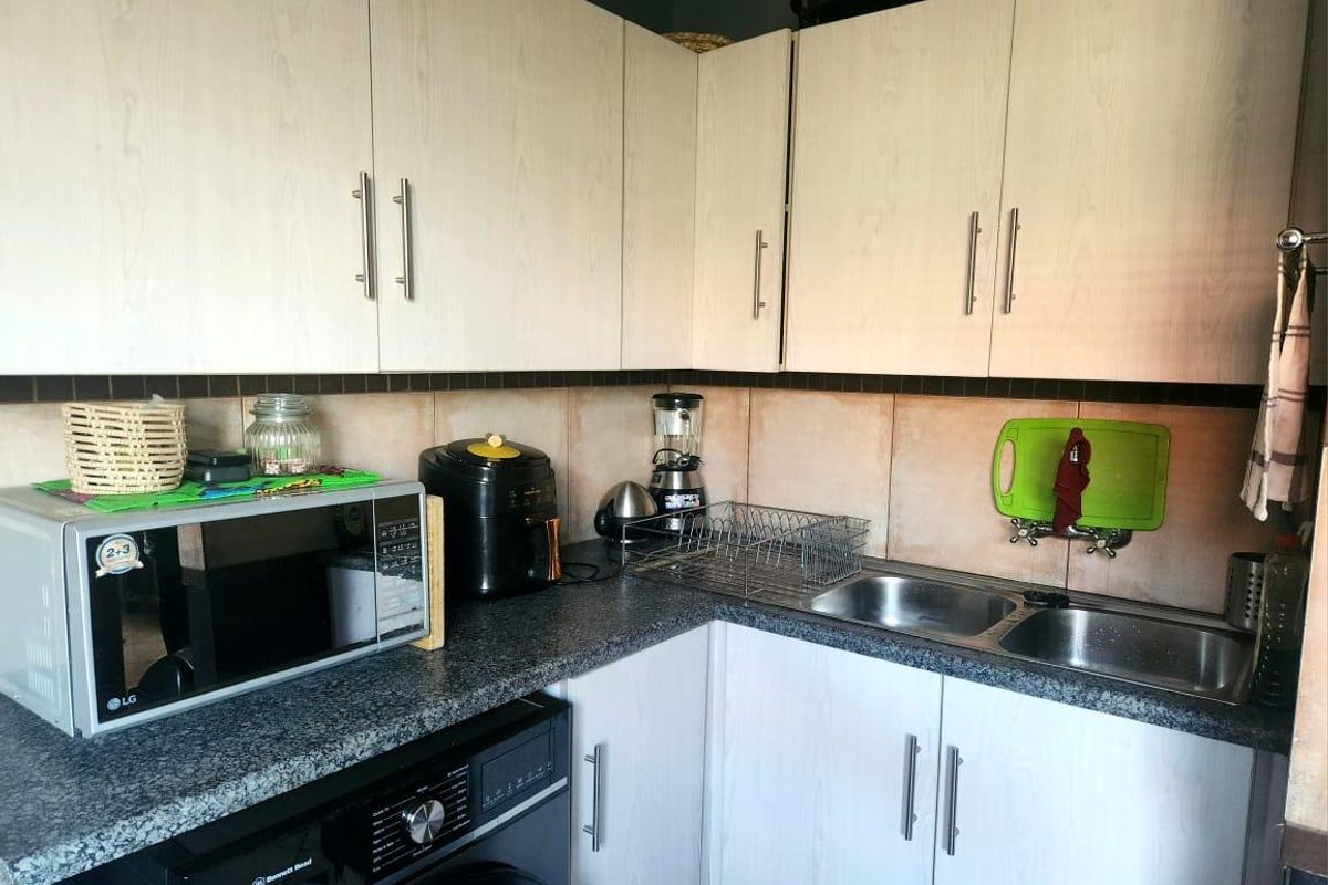 A functional kitchen area featuring light wood-grain cabinetry, granite countertops, a double stainless steel sink, and a built-in washing machine.