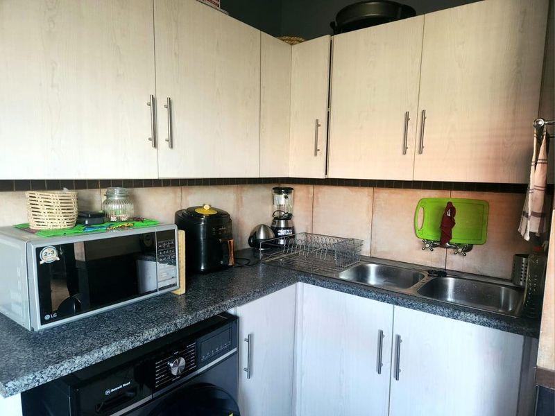 A functional kitchen area featuring light wood-grain cabinetry, granite countertops, a double stainless steel sink, and a built-in washing machine.