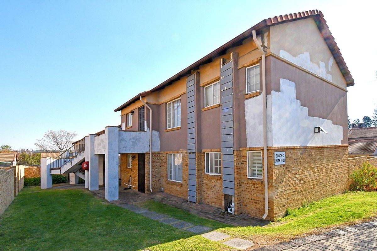 Rear view of a multi-story townhouse block featuring brick and plaster construction, external staircases, and a surrounding lawn area.