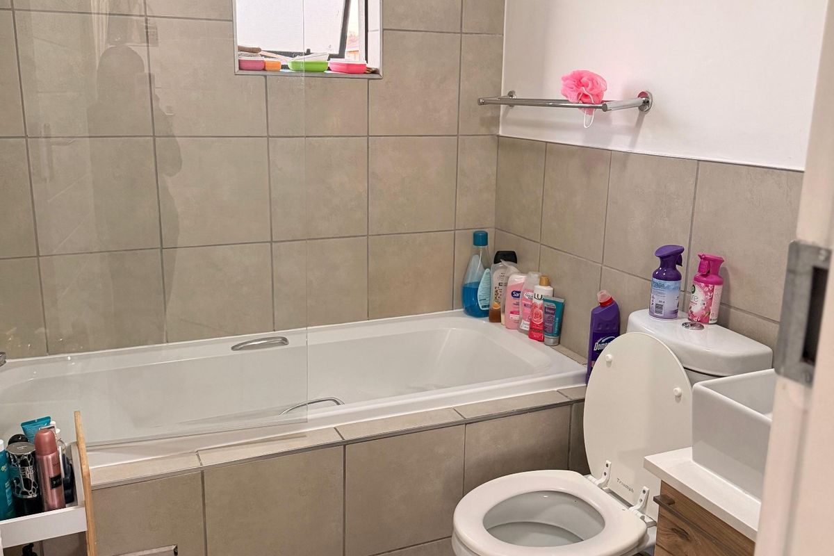 A functional bathroom featuring a bathtub with a glass screen, a toilet, and a vanity unit with a basin, finished with neutral wall tiles.