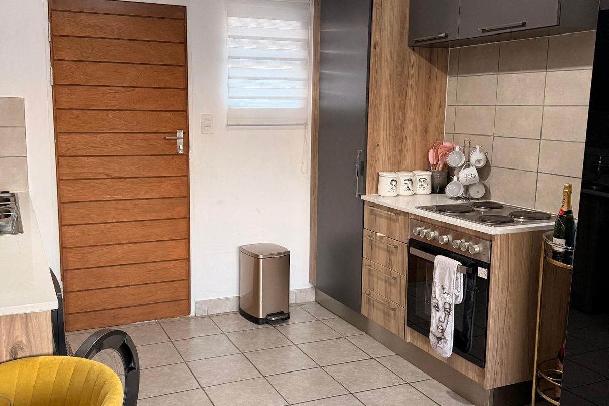 A modern kitchen featuring wood-grain and charcoal cabinetry, a built-in oven with electric hob, tiled flooring, and a neutral tiled backsplash.