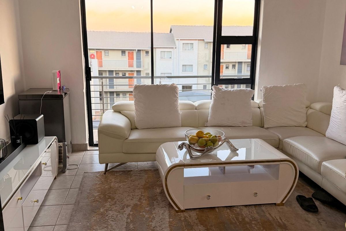 A bright living room featuring tiled flooring and a large sliding glass door that provides access to a balcony with neighborhood views.