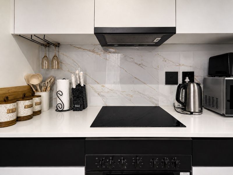 Modern kitchen featuring sleek black and white cabinetry, a marble-look splashback, stone countertops, and integrated electric cooktop with extractor fan.