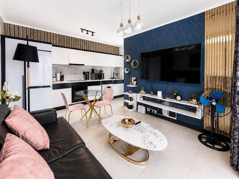 Modern open-plan living area featuring a sleek kitchen with built-in cabinetry, marble-look backsplash, and a striking blue geometric feature wall with integrated shelving.