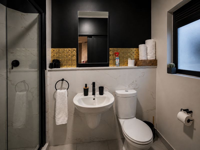 Modern bathroom featuring a wall-mounted basin, toilet, and shower enclosure with contemporary black fixtures and stylish gold-accented tiling.