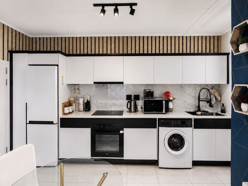 Modern kitchen featuring sleek white and black cabinetry, marble-look splashback, integrated appliances, and contemporary track lighting.