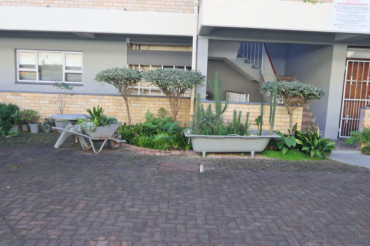 Rear exterior view of the apartment building featuring brick paving, a communal staircase, and a security gate entrance.
