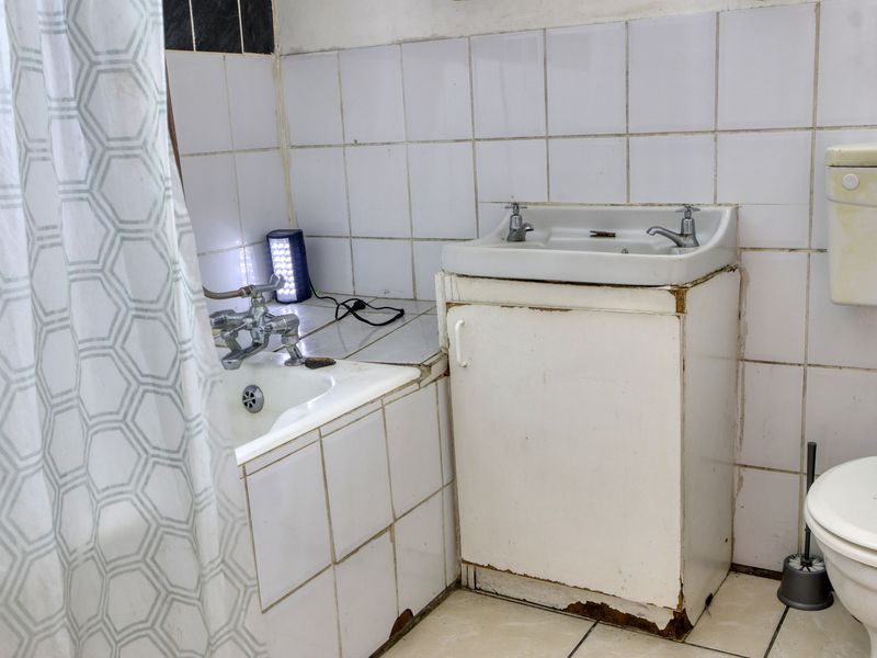 A dated bathroom featuring a tiled bathtub, vanity basin, and toilet, requiring significant renovation and modernization of fixed finishes.