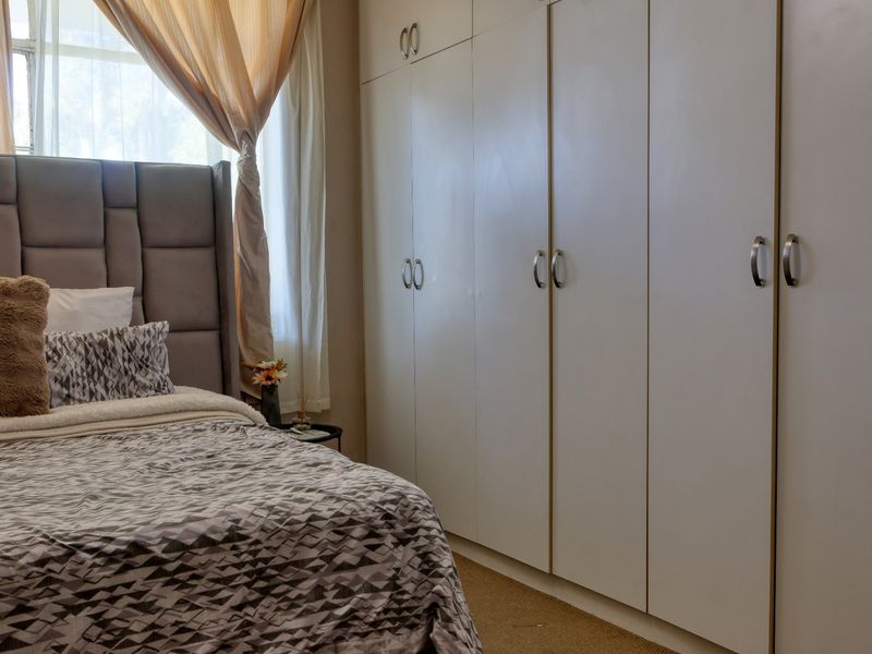 A well-lit bedroom featuring extensive floor-to-ceiling built-in cupboards and a modern upholstered headboard.